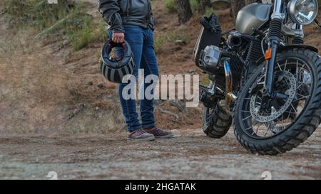 Persona irriconoscibile con casco in mano accanto alla motocicletta parcheggiata Foto Stock