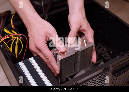 Un uomo a casa raccoglie, disassembla un computer. Le mani di un uomo tengono i fili, collegano i fili. Raccolta di un computer per i professionisti, un computer da gioco Foto Stock