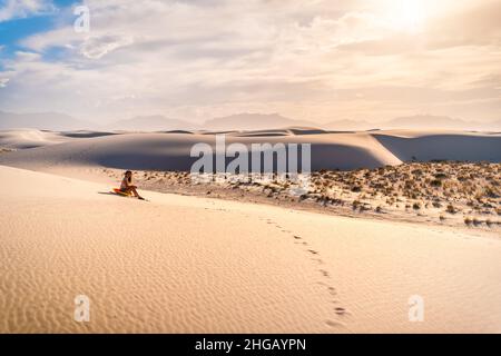 Giovane donna seduta su famose dune di sabbia bianca monumento nazionale in New Mexico su slitta disco per scivolare giù collina durante il tramonto con vintage b Foto Stock