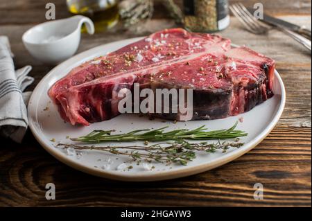 Bistecca di Porterhouse secca invecchiata e cruda con condimento ed erbe aromatiche Foto Stock