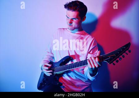 Un uomo suona la chitarra elettrica con luce al neon, luce blu rossa. Hobby, musica, club. Un uomo ama suonare la chitarra, urlare, vivide emozioni. Foto Stock