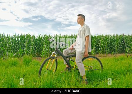 Il ragazzo sullo sfondo del campo di mais si siede su una bicicletta Foto Stock