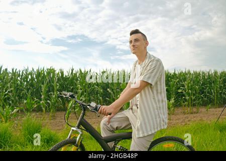 Il ragazzo sullo sfondo del campo di mais si siede su una bicicletta Foto Stock