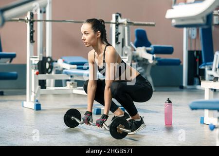 Giovane donna slim in palestra perfoms squats esercizi con un barbell. Concetto di stile di vita sano Foto Stock