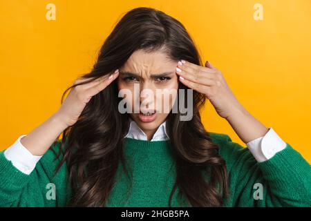 Ritratto di una donna accigliata casual in piedi su sfondo giallo che soffre di un mal di testa Foto Stock