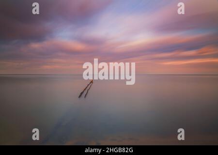 Breakwater che entra in mare all'alba su una spiaggia a Hindeloopen in Olanda. Lo sfondo è un bellissimo cielo colorato. Foto Stock