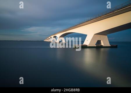 Bellissimo ponte lungo Zeeland che conduce sul mare in Olanda. Foto al tramonto a lungo. Ci sono belle nuvole blu nel cielo. Foto Stock