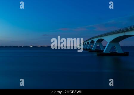 Bellissimo ponte lungo Zeeland. Foto dopo il tramonto a lungo in blu ora. Ci sono belle nuvole blu nel cielo. Foto Stock