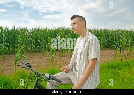 Il ragazzo sullo sfondo del campo di mais si siede su una bicicletta Foto Stock