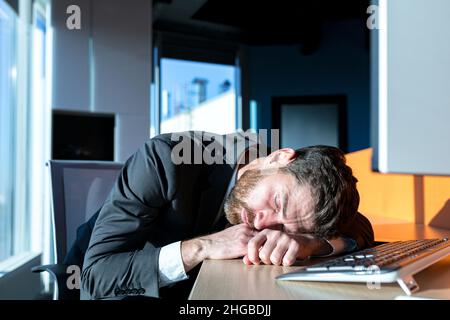 Primo piano di un uomo d'affari, uomo che dorme alla sua scrivania, durante il giorno al computer Foto Stock