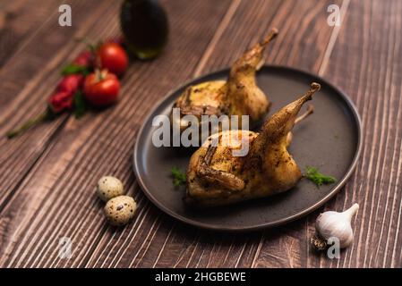 Quaglie tostate intere su un piatto. Quaglie fritte con pomodori, aglio e uova di quaglia Foto Stock