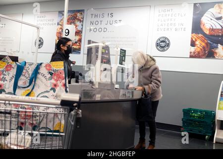 M&S Marks & Spencer negozio cliente shopper shopping bag e donna pagare, lavoratore che lavora al banco cassa con maschera covid 2022 UK Foto Stock