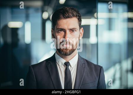 Ritratto di un boss di successo, foto di un uomo d'affari vicino, riuscito e pensivo guardando la macchina fotografica, un uomo con una barba in un ufficio moderno Foto Stock