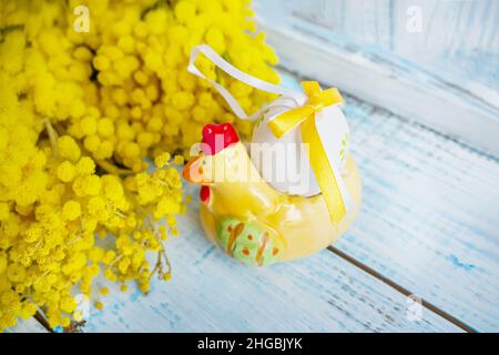 Uovo di Pasqua in ceramica a forma di pollo con fiori di mimosa. Decorazione per il tavolo delle vacanze di Pasqua. Spazio di copia. Foto Stock