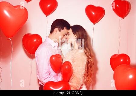 L'uomo con la sua bella ragazza di innamorato bacia al giorno di San Valentino dell'amante. Coppia di San Valentino. Coppia bacio e abbraccio. Su sfondo palloncini rossi cuori. Amore conc Foto Stock