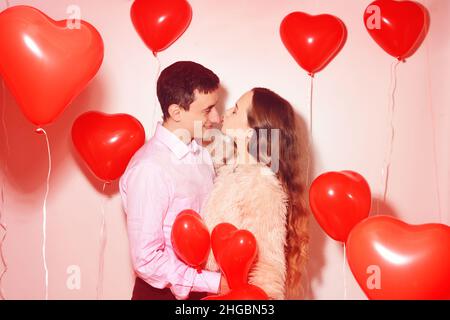 L'uomo con la sua bella ragazza di innamorato bacia al giorno di San Valentino dell'amante. Coppia di San Valentino. Coppia bacio e abbraccio. Su sfondo palloncini rossi cuori. Amore conc Foto Stock