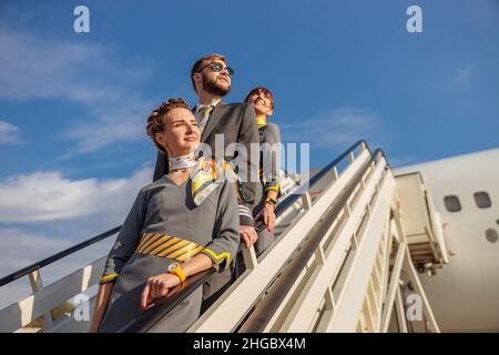 Due donne stewardesses e capitani di aviazione maschile in piedi sulle scale di imbarco aerei sotto il cielo blu Foto Stock