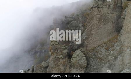 Montagne maestose nelle nuvole con alberi gialli e autunnali. Paesaggio con belle alte rocce e drammatica nebbia con alberi gialli, sfondo naturale. Foto Stock