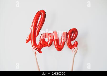Ama palloncino rosso in mani femminili. Buon San Valentino, Festa della mamma, concetto di compleanno. Foto Stock