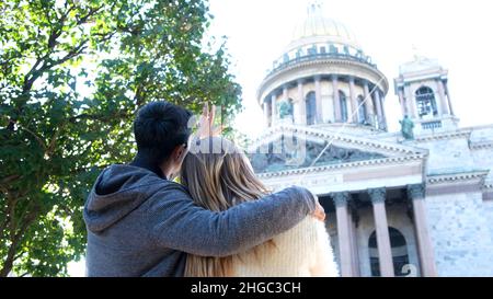 Vista posteriore di una coppia felice in piedi e discutere incredibile tempio vicino verde cespuglio. Uomo che abbraccia la donna, guardando la bella Cattedrale e indicando un f Foto Stock