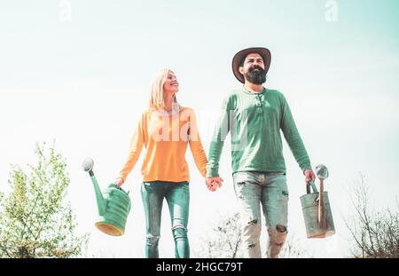Piante e giardinaggio come hobby di primavera. Concetto di lavoro di squadra e amicizia. Coppia felice di agricoltori che trasportano pala un annaffiatoio su un sole Foto Stock
