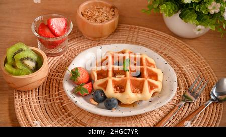 Un piatto di gustosi waffle con frutti di bosco freschi, una tazza di kiwi fresco, fragole e muesli sul tavolo. Foto Stock