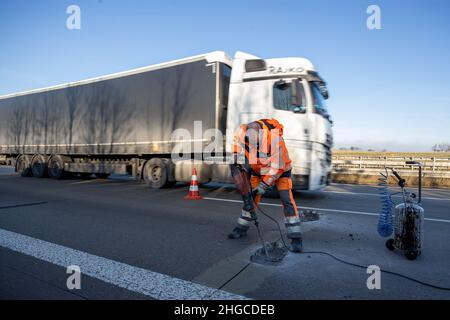 Dresda, Germania. 19th Jan 2022. Un dipendente della Autobahn GmbH utilizza un martello di cianfrinatura per aprire l'area danneggiata sulla carreggiata della A4 vicino a Dresda, mentre un camion passa sullo sfondo a più di 80 km/h. L'area danneggiata viene quindi riparata con una miscela minerale in modo che il traffico possa rifluire. Questo punto è quindi patch con una miscela minerale in modo che il traffico possa fluire di nuovo. Credit: Daniel Schäfer/dpa-Zentralbild/dpa/Alamy Live News Foto Stock