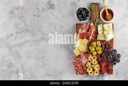 Vista dall'alto di gustosi salumi con formaggio, uva, noci, olive e prosciutto su un piatto da cucina circolare Foto Stock