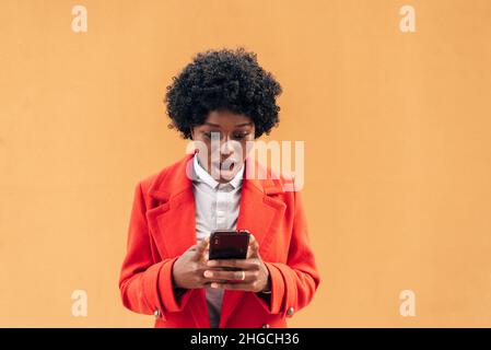 Scioccata donna afro guardando sorpreso il suo telefono cellulare. Foto Stock