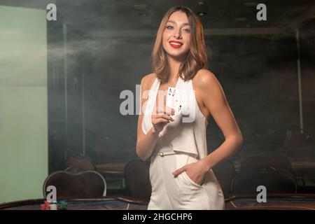 Giovane donna sorridente che mostra un paio di assi nella stanza vuota del casinò Foto Stock