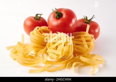 Primo piano di pasta non cotta e pomodori freschi maturi isolati su sfondo bianco Foto Stock