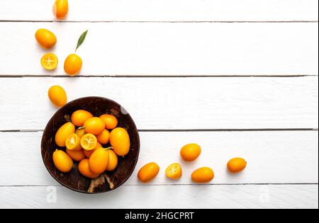 Kumquats o cumquats ( Citrus japonica) all'interno di una ciotola di cocco e su sfondo di legno bianco. Concetto di cornice di agrumi alimentari bordo. Foto Stock