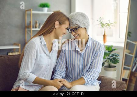 Felice amorevole madre anziana e figlia cresciuta seduto sul divano, tenendo le mani e sorridendo Foto Stock