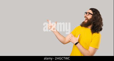 Ehi, guarda questo. L'uomo bearded eccitato che punta all'angolo sopra lo sfondo grigio. Foto Stock