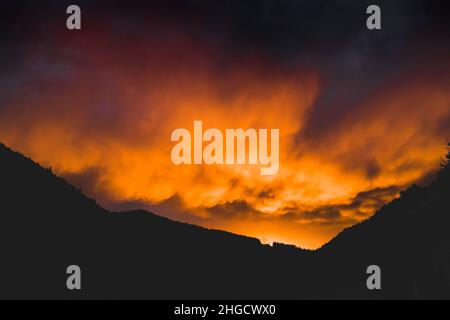 Epico cielo arancione tramonto con nuvole minacciose nelle montagne dei Vosgi con una linea di alimentazione pilone in Francia Foto Stock