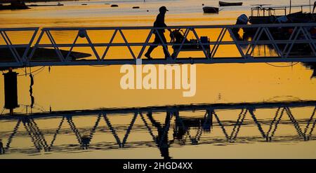 Poole, Regno Unito. 20th Jan 2022. Un pescatore si dirige per la sua barca mentre il Sole sorge sopra Poole Harbour nel Dorset all'inizio di un'altra bella, soleggiata e fredda giornata invernale. Credit: Richard Crease/Alamy Live News Foto Stock