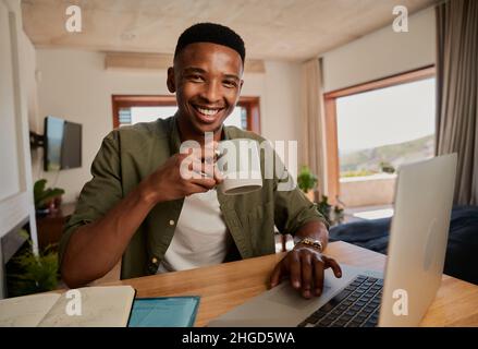 Ritratto di giovane adulto nero maschio tenendo la tazza, sorridendo alla macchina fotografica. Lavorare a distanza in un appartamento moderno. Foto Stock