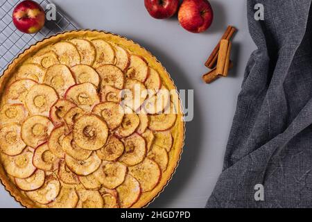 Vista dall'alto della crostata classica francese di mele su sfondo grigio con mele e bastoncini di cannella Foto Stock