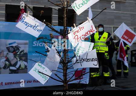 29 dicembre 2021, Sassonia-Anhalt, Halle (Saale): Dimostrazione dei vigili del fuoco in stand di abbigliamento professionale con una bandiera e bandiere Ver.di davanti al Ratshof. Davanti a loro è un albero di Natale bruciato giù con le richieste formulate. Protestano contro le "misure di riduzione dei costi" e la mancanza di apprezzamento. Foto: Kevin Meyer/dpa-Zentralbild/dpa Foto Stock