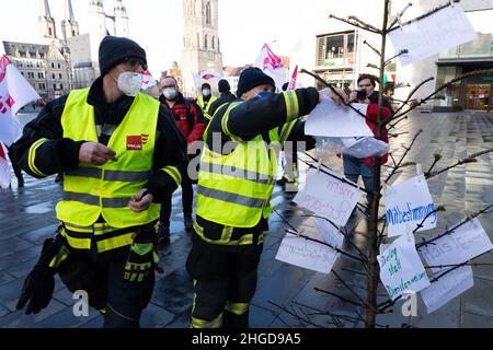 29 dicembre 2021, Sassonia-Anhalt, Halle (Saale): Due vigili del fuoco in uniforme appendere note con richieste alla città su un albero di Natale bruciato di fronte al Ratshof. Protestano contro le "misure di riduzione dei costi" e la mancanza di apprezzamento. Foto: Kevin Meyer/dpa-Zentralbild/dpa Foto Stock