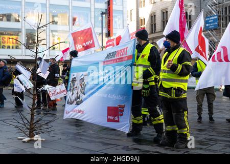 29 dicembre 2021, Sassonia-Anhalt, Halle (Saale): Dimostrazione dei vigili del fuoco in stand di abbigliamento professionale con una bandiera e bandiere Ver.di davanti al Ratshof. Davanti a loro è un albero di Natale bruciato giù con le richieste formulate. Protestano contro le "misure di riduzione dei costi" e la mancanza di apprezzamento. Foto: Kevin Meyer/dpa-Zentralbild/dpa Foto Stock