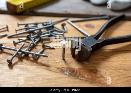 Pinze e chiodi impilati su legno. Tavolo da lavoro da carpentiere, vista closeup, laboratorio di Falegnameria Foto Stock