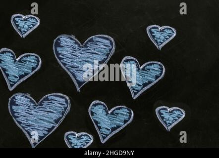 Disegno del cuore sulla lavagna della scuola. Amore, San Valentino simbolo. Un gruppo di cuori di colore blu disegnati a mano di varie dimensioni su tavola nera Foto Stock