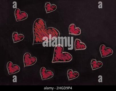 Disegno di cuore rosso sulla lavagna della scuola. Amore, San Valentino simbolo. Un gruppo di cuori disegnati a mano disegno di varie dimensioni su tavola nera Foto Stock