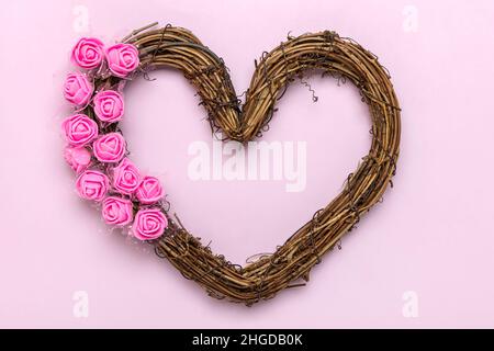 Corona di rattan a forma di cuore decorata con fiori rose su sfondo rosa Vista dall'alto Flat Lay Holiday Card buon San Valentino, amore concetto Copia spa Foto Stock