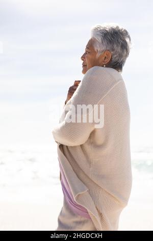 Vista laterale della donna anziana biraciale con capelli bianchi corti che indossano un tappeto sulla spiaggia in giornata di sole Foto Stock