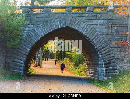 La gente gode di camminare su un sentiero sotto lo storico ponte di pietra sulla strada carrozza nel Parco Nazionale di Acadia, Maine, USA Foto Stock