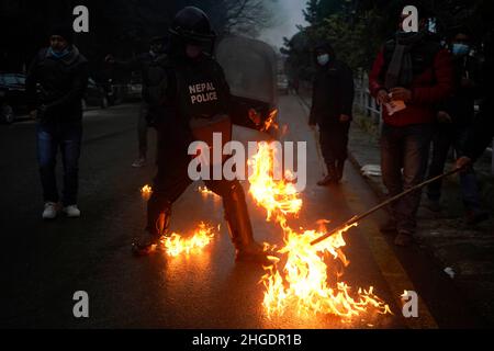 Kathmandu, Nepal. 20th Jan 2022. Un poliziotto riota tenta di destare un fuoco acceso dai quadri del Partito Comunista del Nepal durante una protesta contro l'aumento dei prezzi del carburante a Kathmandu, Nepal, giovedì 20 gennaio 2022. (Credit Image: © Skanda Gautam/ZUMA Press Wire) Foto Stock