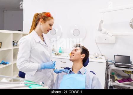 La dottoressa rossa tocca la spalla e sorride al giovane mentre lavora nella moderna clinica dentale Foto Stock