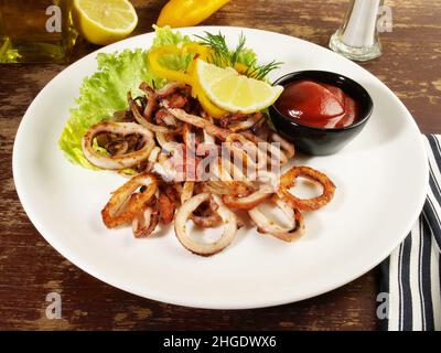 Polpo, Calamari fritti anelli con insalata su un piatto con salsa al peperoncino e limone Foto Stock